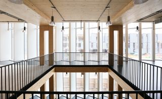 Daytime image of the Sky Health & Fitness Centre, Black rail viewing gallery, wooden framed balcony and pillars, white framed tall windows looking out to the surrounding building, bulb lights hanging down from the ceiling, lower floor windows visible