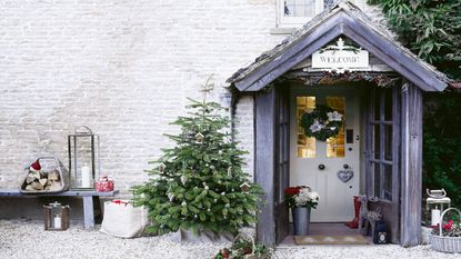 Christmas tree outside a house front door with snow covering the tiles and floor