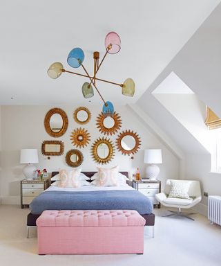 An example of bedroom chandelier ideas showing a bedroom with a sputnik chandelier with multicolored lamps above a blue bed and pink upholstered storage box