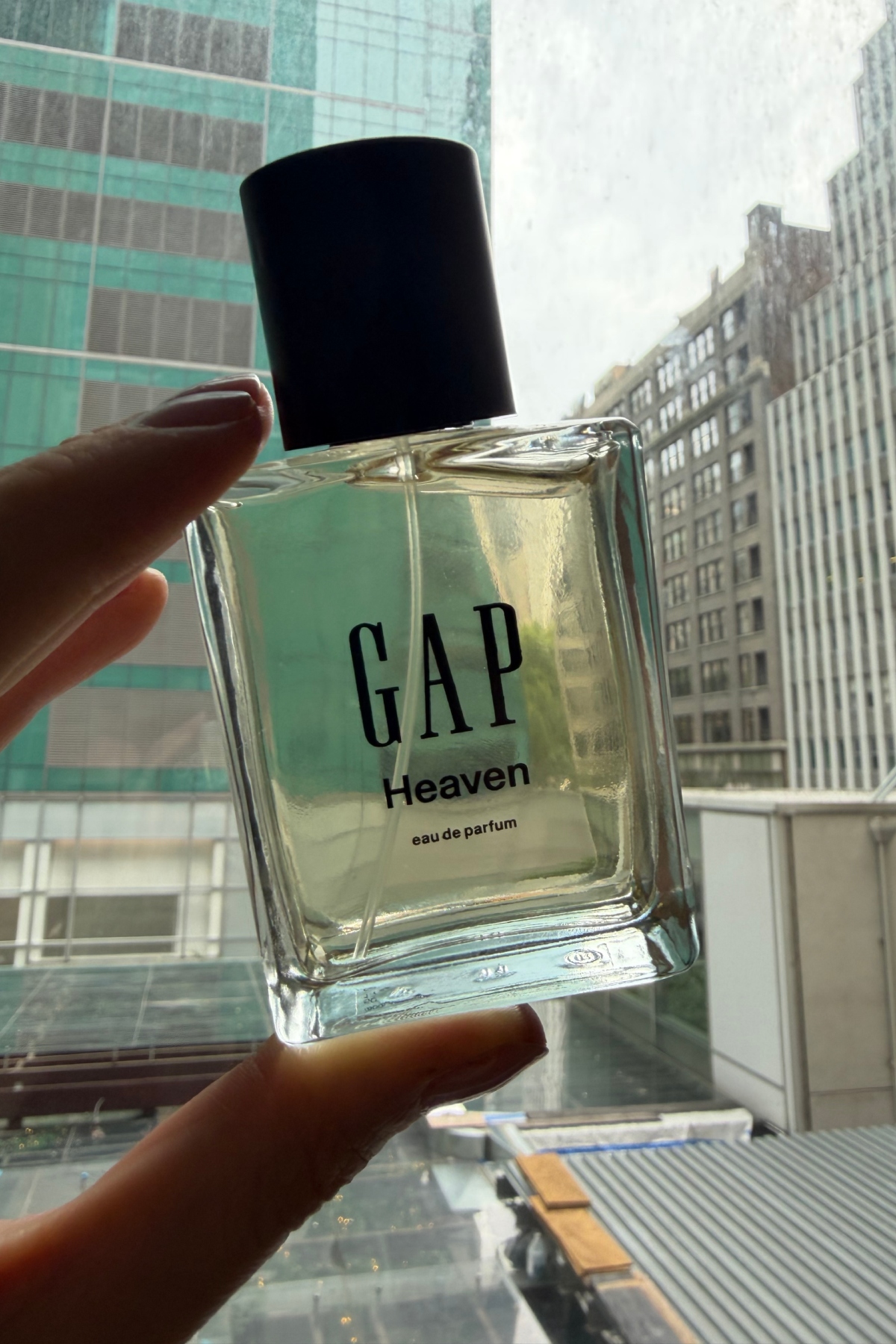 a hand holding up a clear glass bottle of Gap Heaven perfume to the window