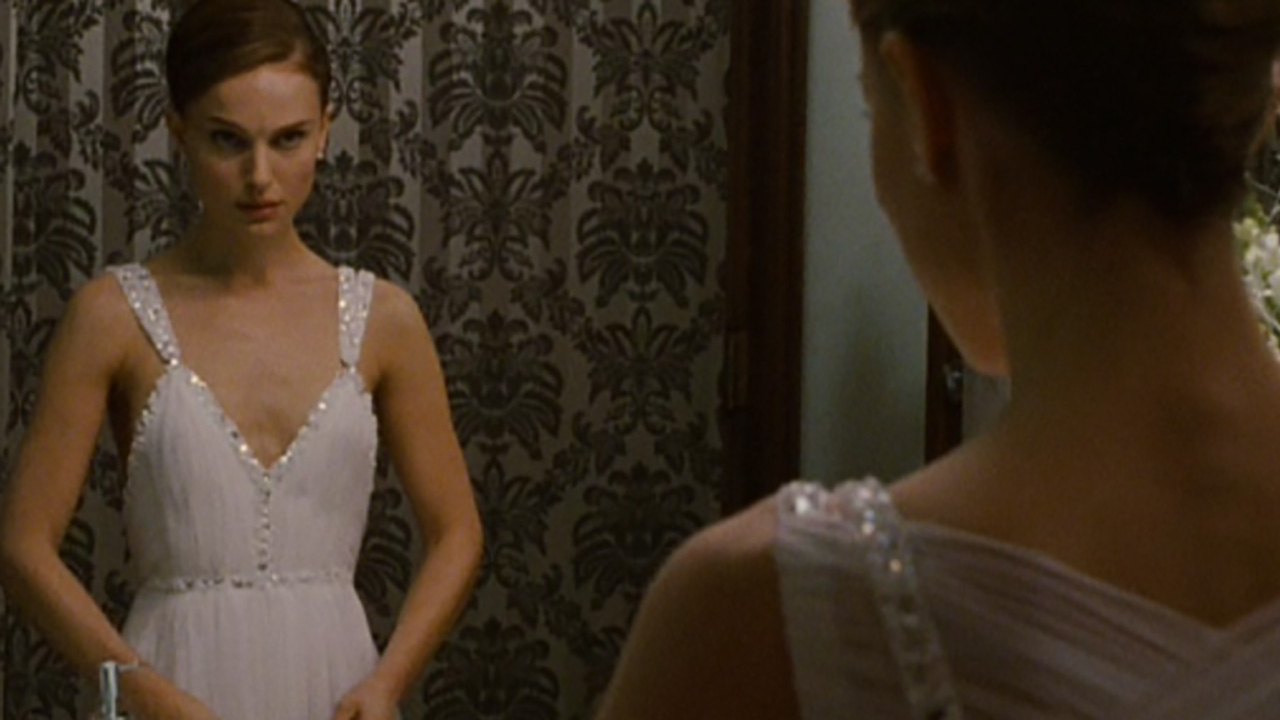 Natalie Portman wears a white gown and looks in the mirror in Black Swan.