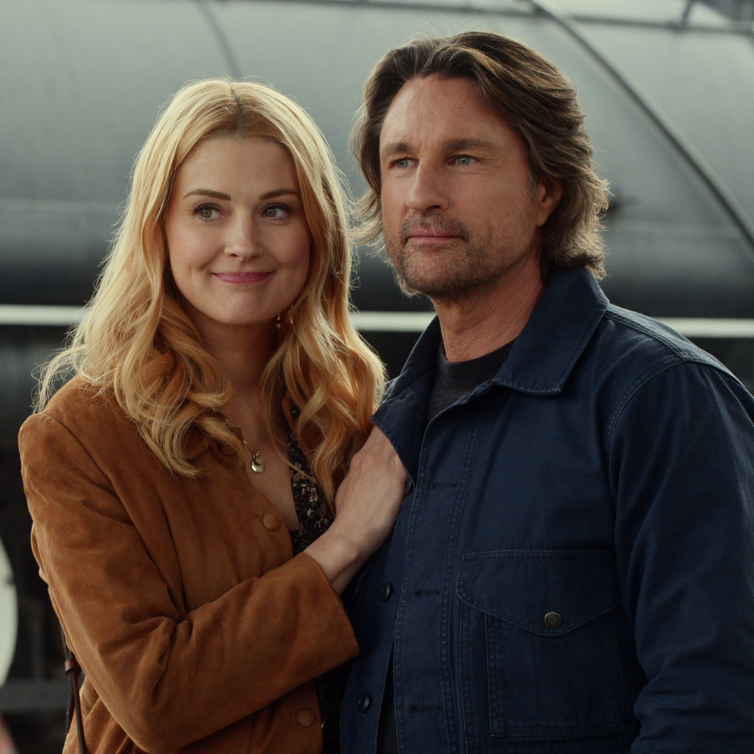 alexandra breckenridge as mel and martin henderson as jack embrace in front of a train at a train station while meeting a mysterious woman in a new still from virgin river season 7