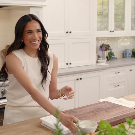 Meghan Markle in the kitchen smiling and wearing a beige outfit