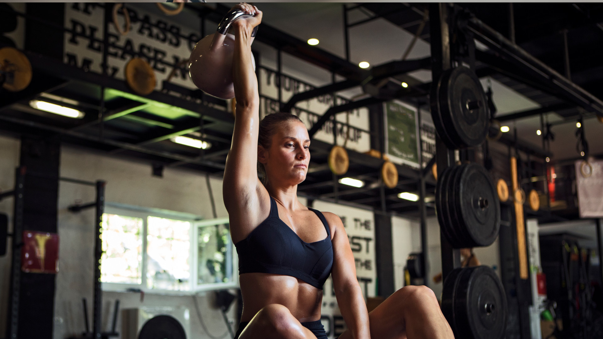 A woman performing an overhead kettlebell press sat on the floor
