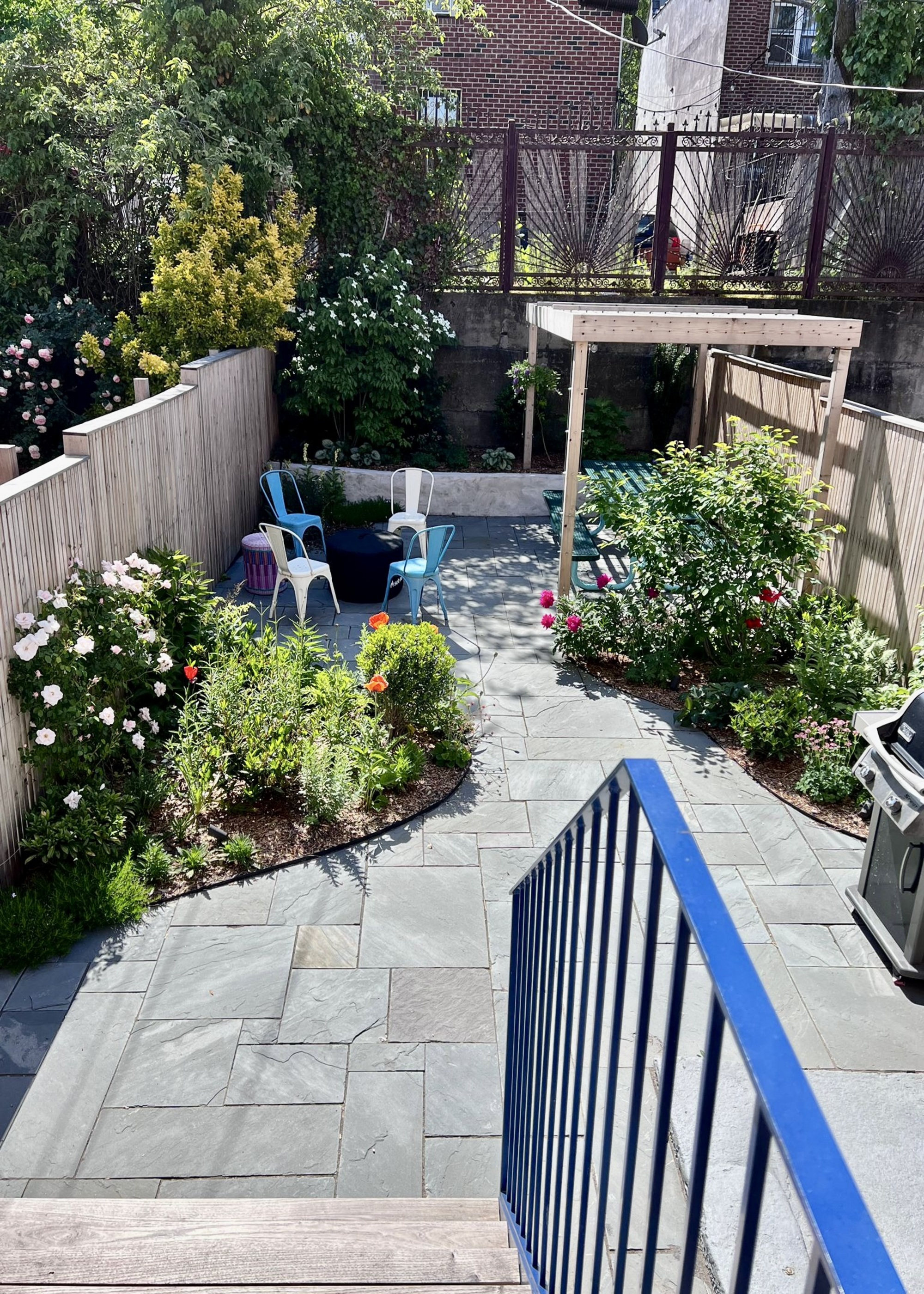 A small backyard with pavers, asymmetrical flower beds, and a small pergola trellis