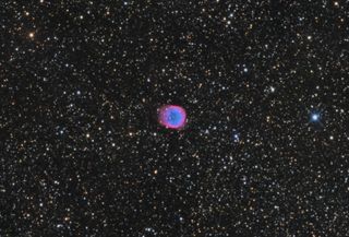 The planetary nebula NGC 6781 is located in the constellation Aquila. It has a pink and blue glow due to the hydrogen and oxygen gases being released by the dying star at the center of the nebula.