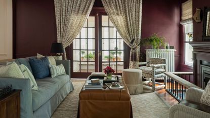 dark reddy purple color drenched living room dressed with a light blue skirted couch, skirted leather ottoman, floral armchairs and floral drapes