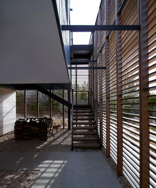 The outside stairway at the beach house has a half-open wall to the right, made out of wooden boards that are evenly spaced out.