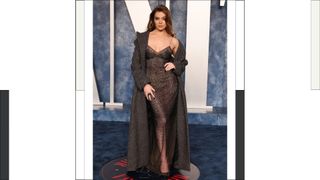Hailee Steinfeld wears a long black sheer shimmery dress and a long coat as she attends the 2023 Vanity Fair Oscar Party Hosted By Radhika Jones at Wallis Annenberg Center for the Performing Arts on March 12, 2023 in Beverly Hills, California.
