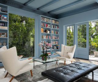 A light blue sitting room with two opposing white high back chairs and black upholstered ottoman