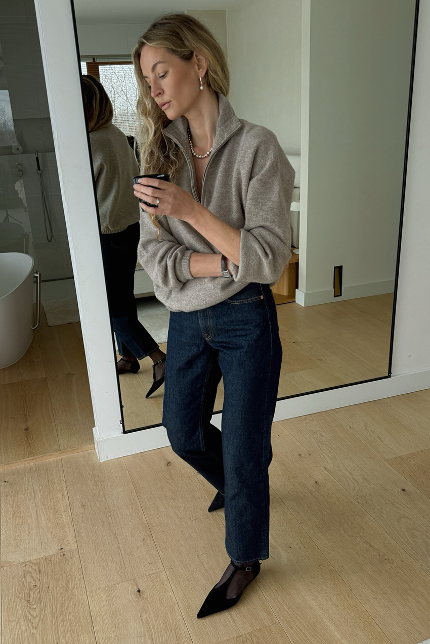 a woman wearing a gray quarter zip, blue indigo jeans, and black T-strap flats