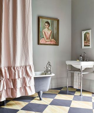 bathroom with gray wall, checkered floor, roll-top bath with pink ruffled shower curtain and artwork on walls