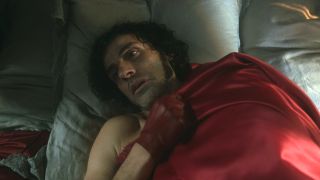 Oscar Isaac in bed with red gloves in Frankenstein