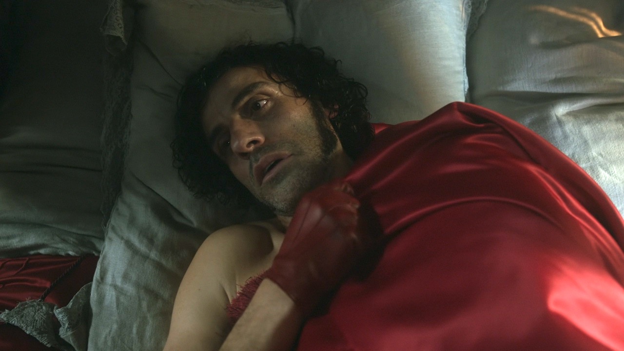 Oscar Isaac in bed with red gloves in Frankenstein