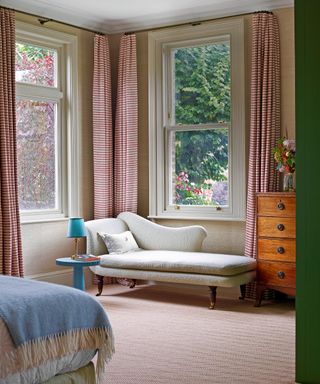 bedroom with off white chaise, red patterned curtains and wooden chest of drawers