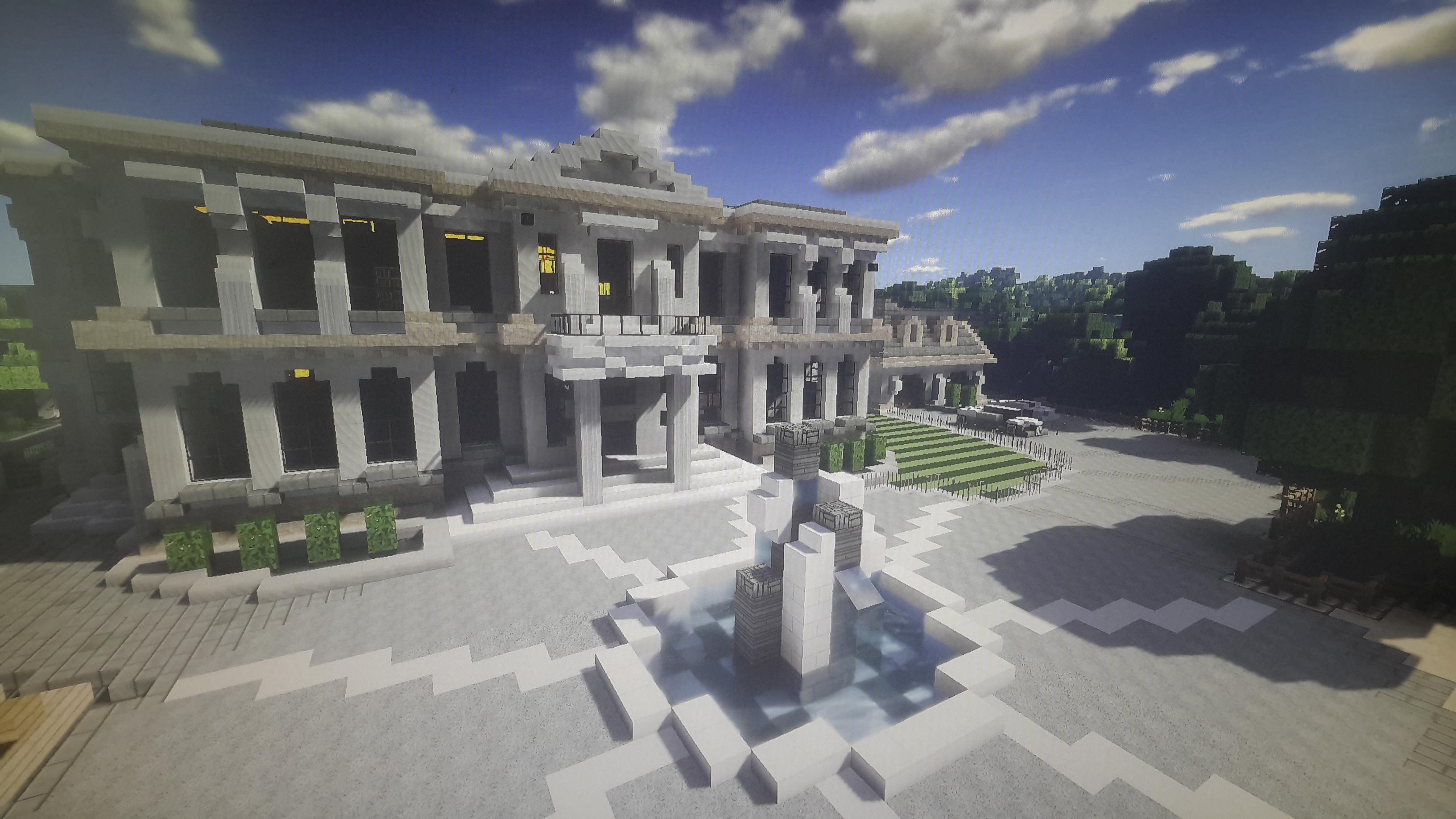 A Minecraft mansion build from stone with a courtyard and a fountain in front.