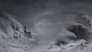 Black-and-white landscape photograph of Porthcawl Lighthouse being battered by crashing waves during a storm 