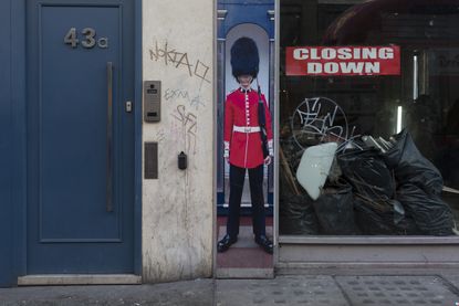 The squashed perspective of a grenadier guardsman standing as sentry next to a doorway and a closed down business - a metaphor for Brexit, on Oxford Street, on 12th December 2017, in London E