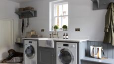 A grey mudroom laundry area with two washing appliances, butlers sink and bench