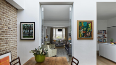 a kitchen with white walls, art hanging, a brick accent wall, and a small table with a vase of flowers on top