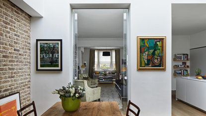a kitchen with white walls, art hanging, a brick accent wall, and a small table with a vase of flowers on top