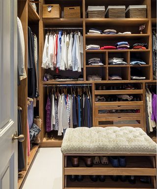 Walk in wardrobe with hanging rails and ottoman with shoes in center