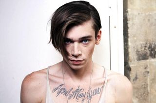 male model with long fringe and chest tattoo under thin vest