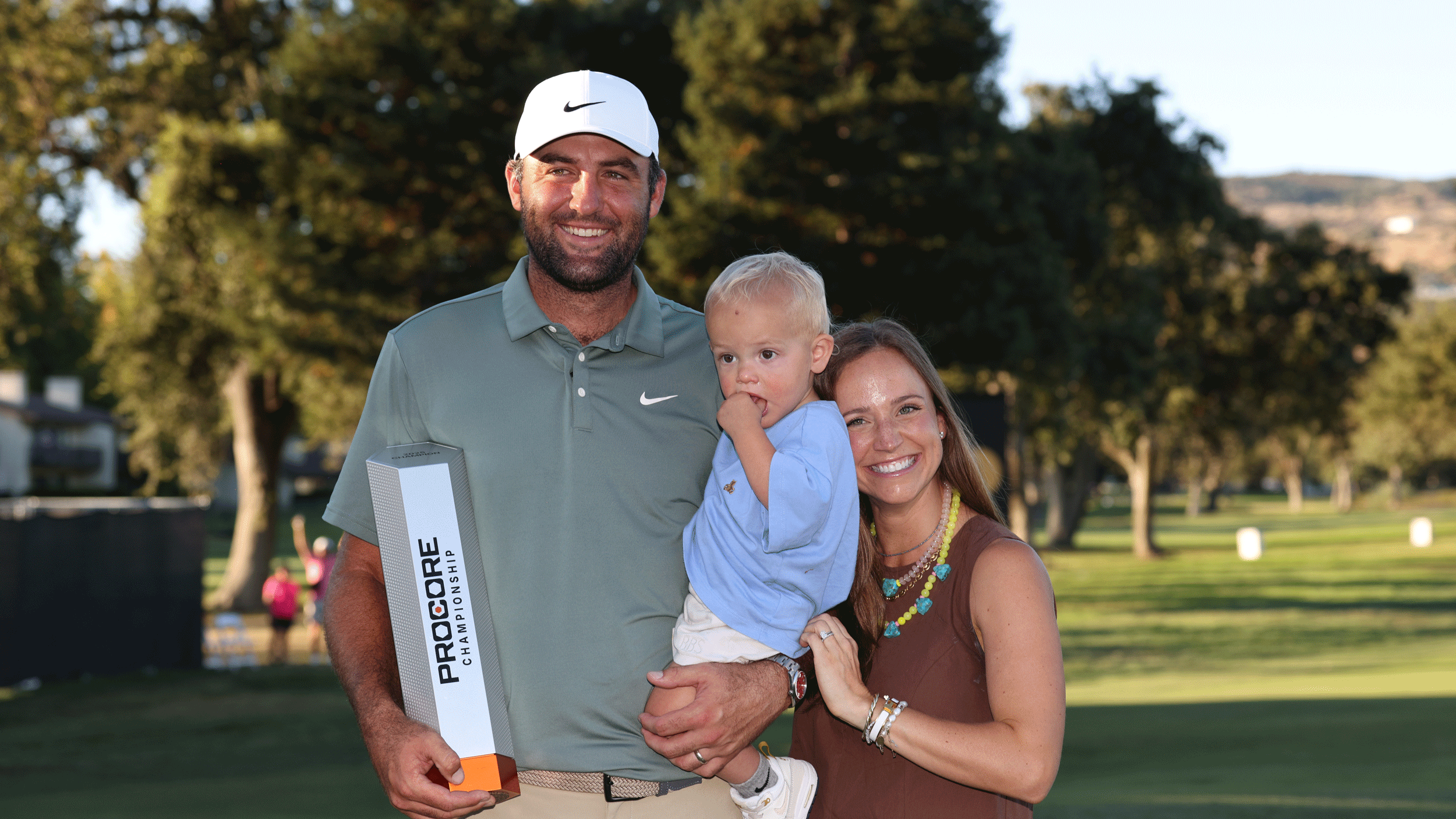 Scottie Scheffler holds son Bennett and the Procore Championship trophy as wife Meredith leans in