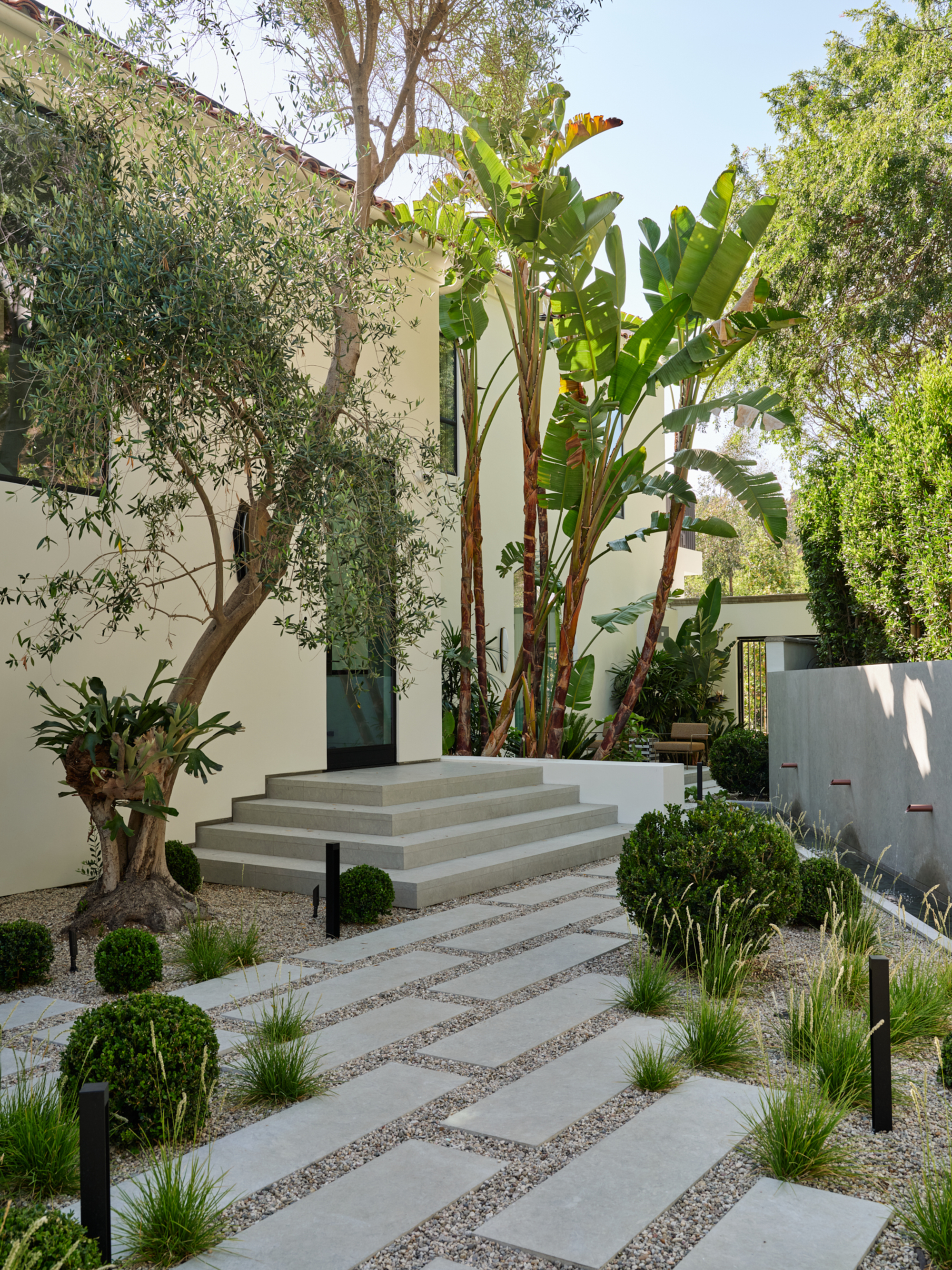Image of the exterior of a large home that is painted in an off-white color and surrounded by plants.