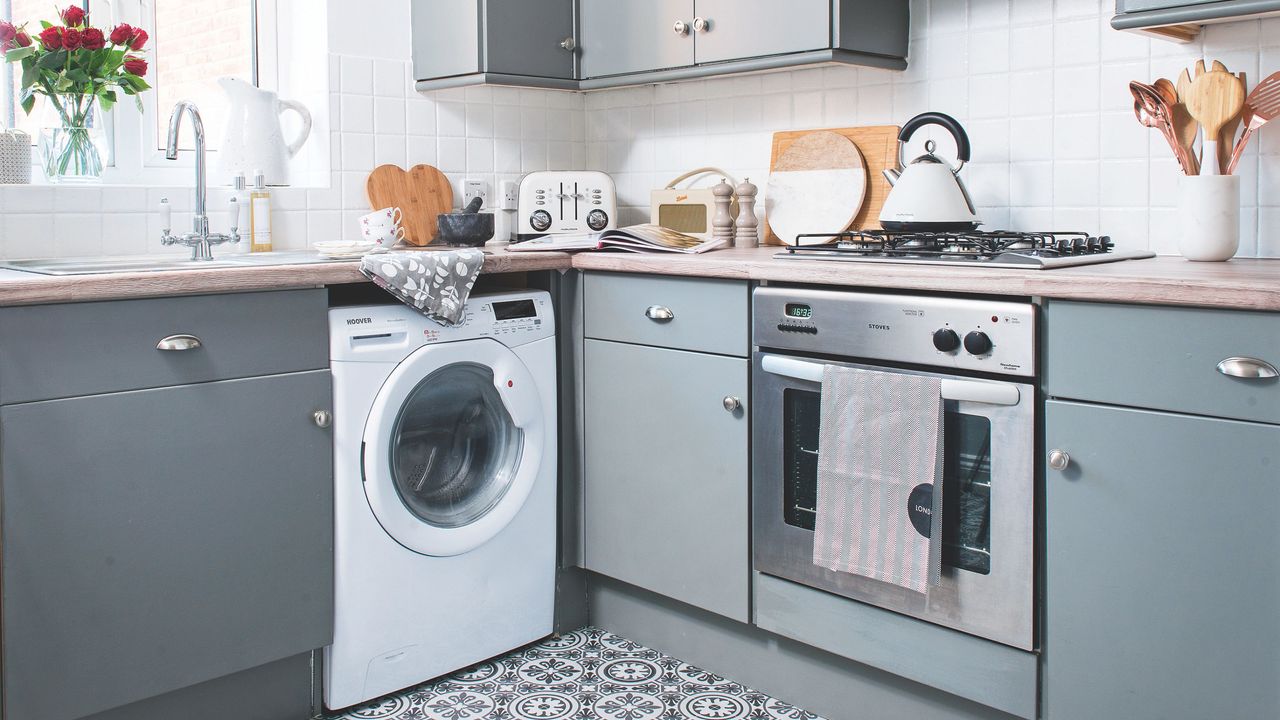 White washing machine in a white kitchen with grey cabinets and grey tiled floor