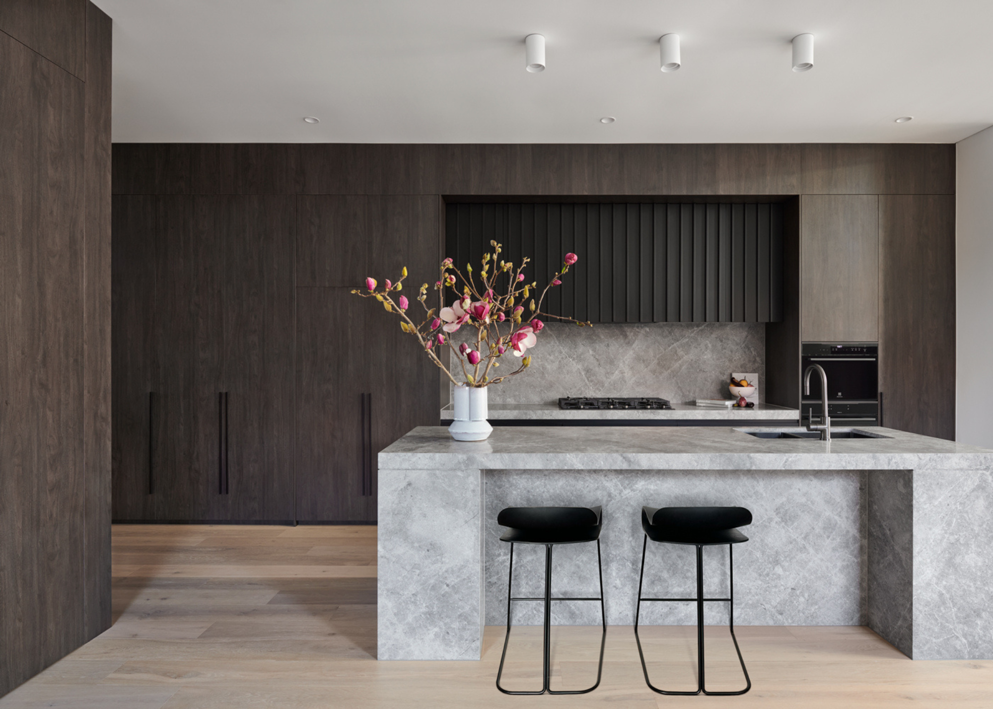 A contemporary dark wood kitchen with floor to ceiling cabinetry and a concrete effect block island in light grey
