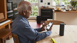 A senior male sits at a table indoors and looks at his smartphone.