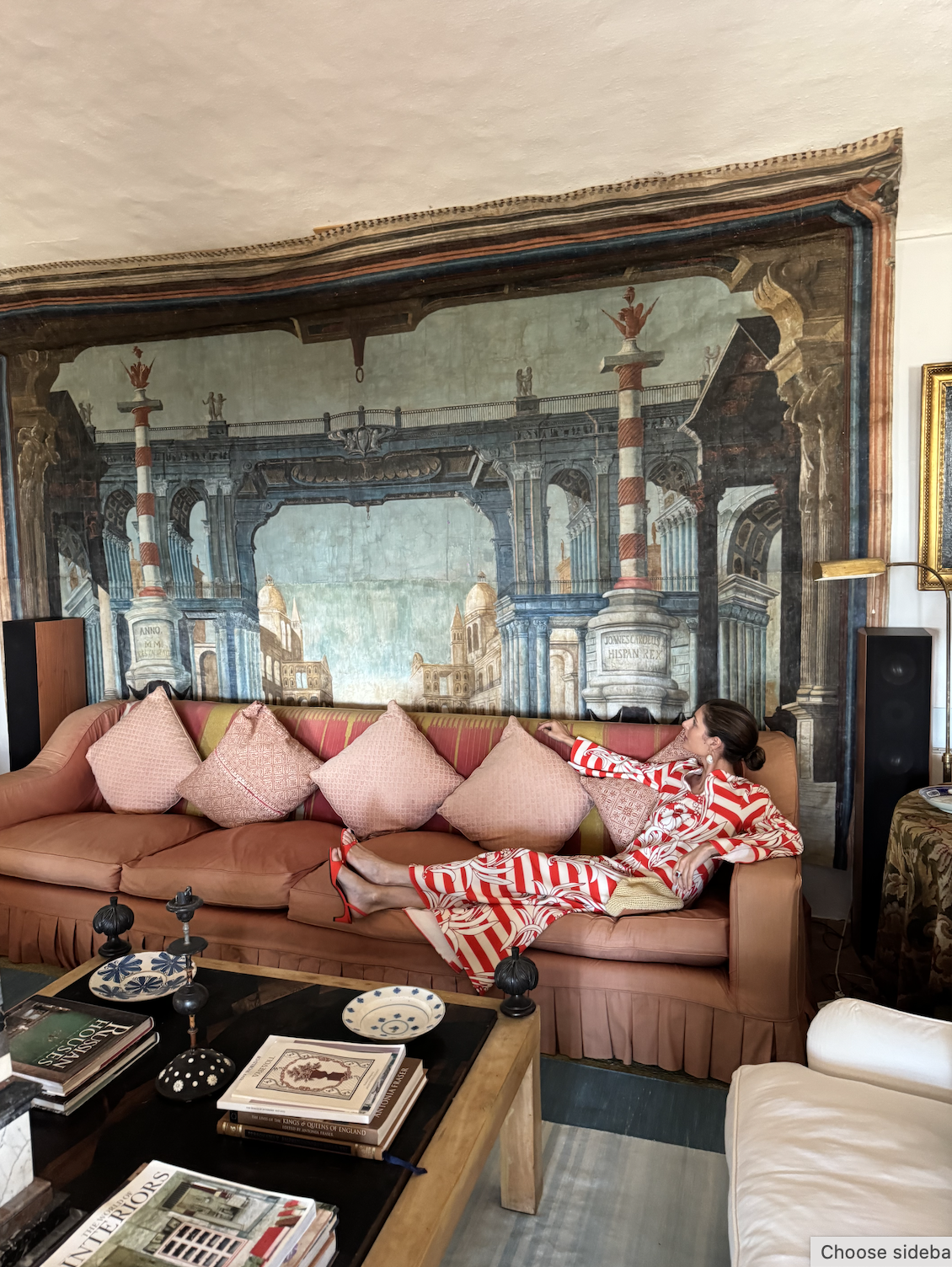 Maria del a Orden wears a stripy red dress and lounges on a red sofa with high heels on