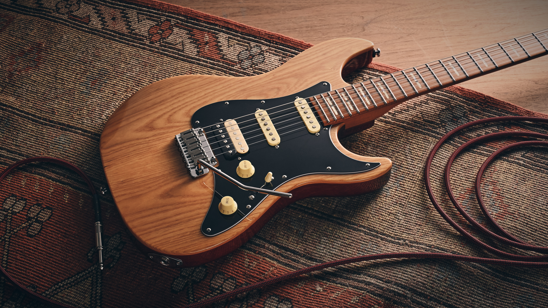 A Sire Larry Carlton S7 Ash Top electric guitar lying on a rug with a guitar cable coiled nearby