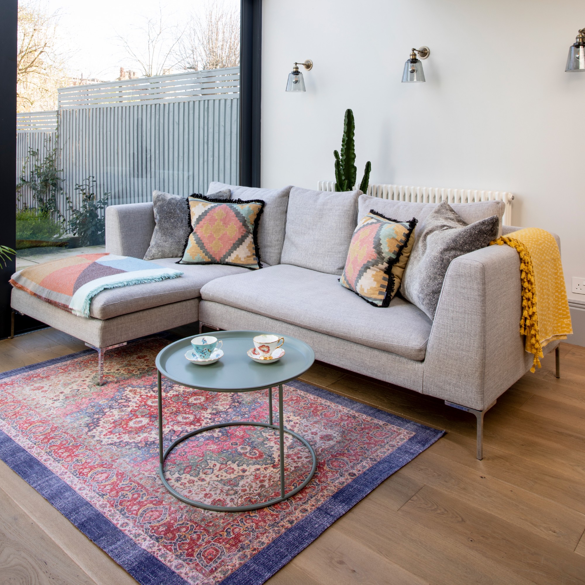 A living room with a grey chaise sofa and a colourful patterned rug underneath it