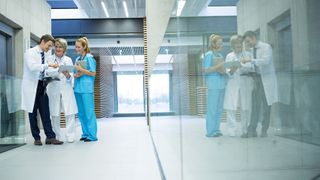 Three doctors in a hospital corridor cheerfully looking at some data on a tablet