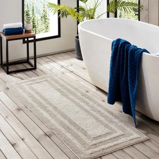 Eddie Bauer Logan Cotton Bath Rug Runner next to a white curved freestanding tub. A dark blue towel draped over the side.