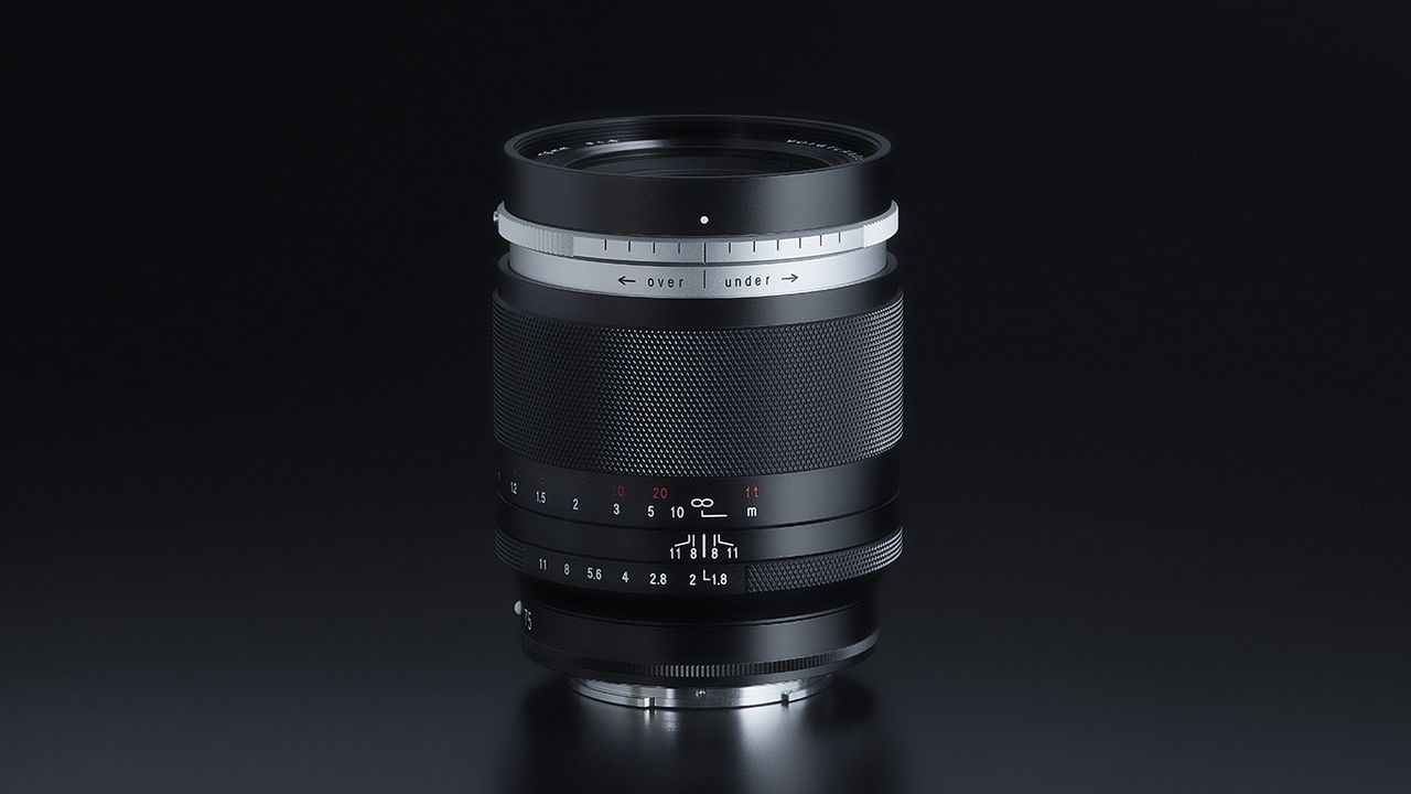 A sleek black camera lens (Voigtlander Portrait Heliar 75mm f/.8) with textured grip and aperture markings displayed, set against a dark background