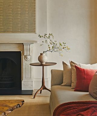 Living room with sleek wooden side table, cream sofa, orange scatter cushions, fireplace in background