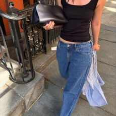 A woman walking down the street in blue baggy jeans and a simple black vest
