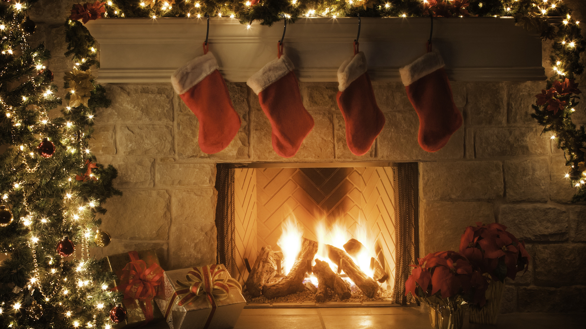 Four red Christmas stockings hanging above a roaring log fire