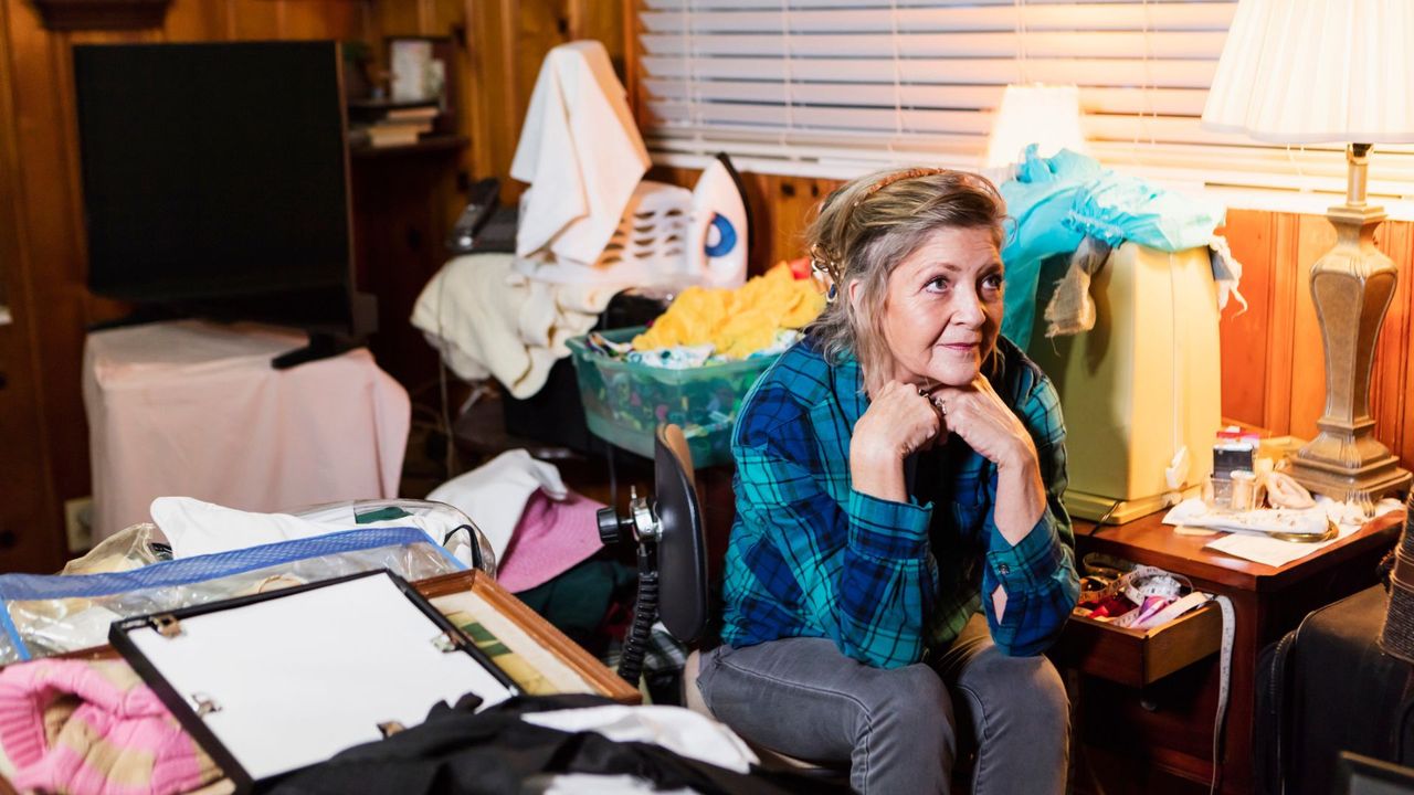 A woman stares despondently surrounded by a messy collection of items