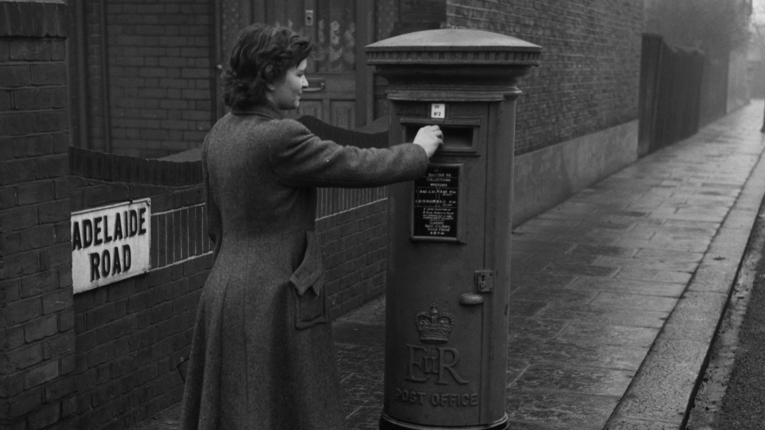 A vintage photograph of a woman posting a letter at a post box