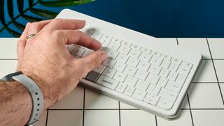 using the touch gestures on a white, lightweight tablet keyboard made by mokibo rests upon a white tiled table with a blue background