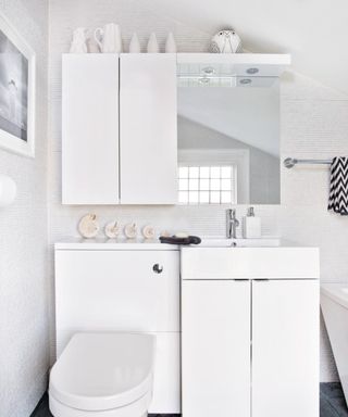 A white bathroom with a toilet with white cabinets and a mirror above it