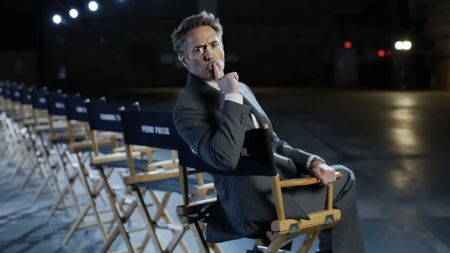 In a director's chair, a grey-suited Robert Downey Jr. shushes the camera as Marvel reveals the Doomsday cast.