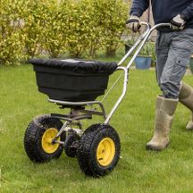 The lower half of a man pushing a fertilizer spreader across a lawn