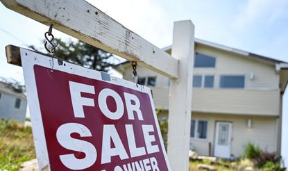 A "For Sale" sign is seen in front of a house. 