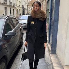 Parisian woman wears a fur stole, black coat and black knee high boots.