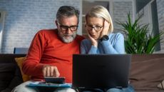 A man and a woman sitting on a couch and the woman has a laptop on her lap